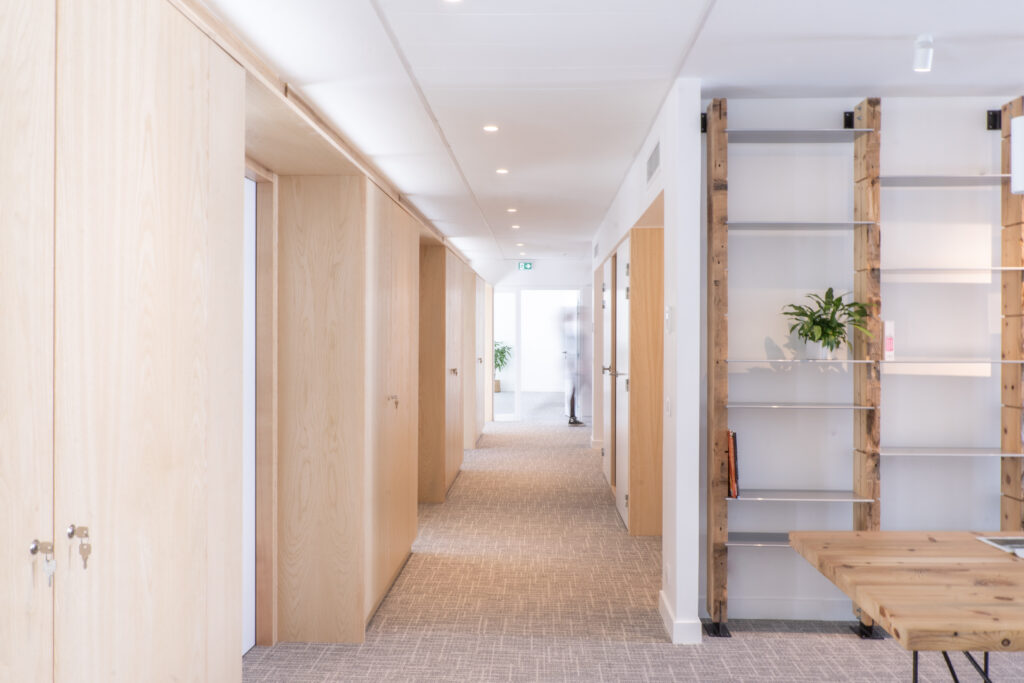 Couloir de bureaux avec menuiseries intérieures en matériaux de réemploi, offrant une esthétique durable et élégante, tout en favorisant la lumière naturelle et l’intimité des espaces de travail